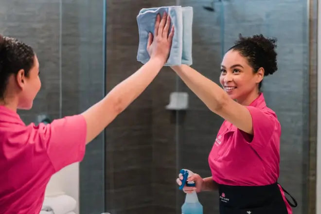 Molly Maid professional wiping a mirror in a bathroom.