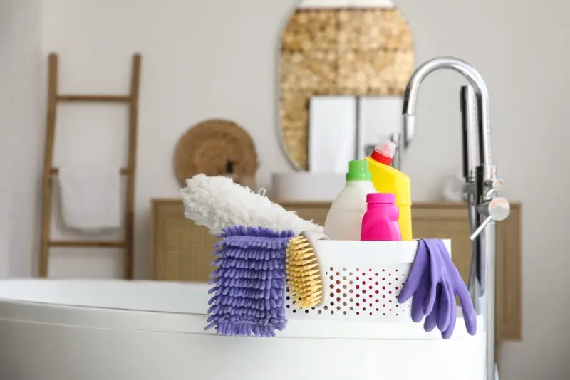 Plastic basket with cleaning supplies on a bathtub.