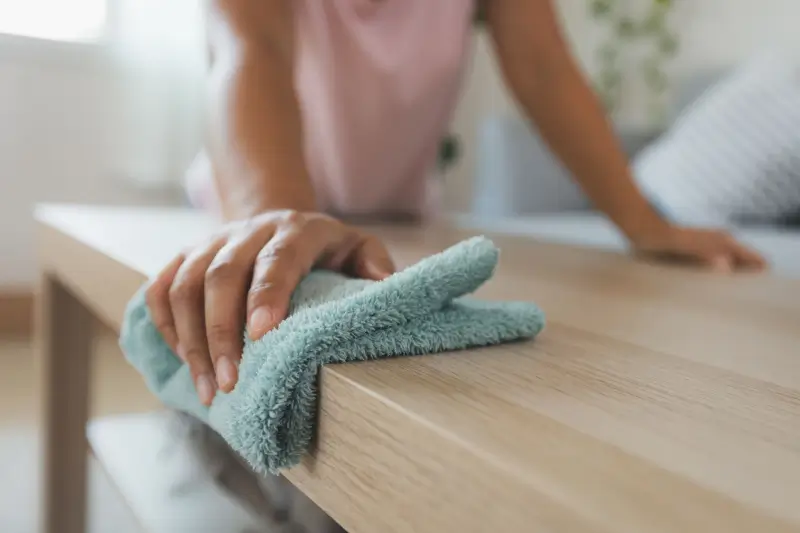 Person wiping coffee table in living room.
