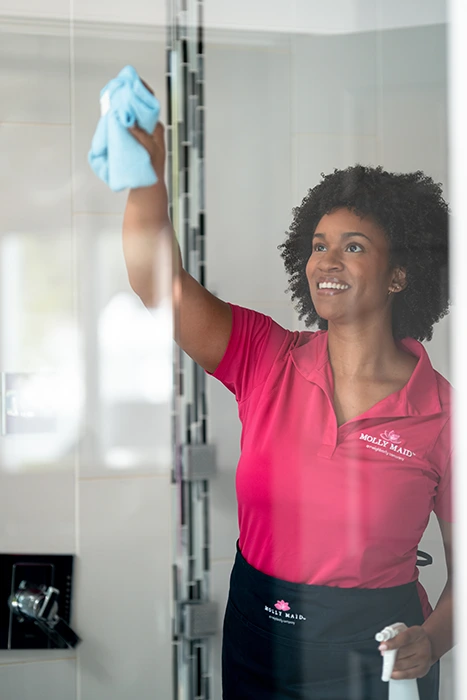 A Molly Maid professional wiping a shower door at a move-out cleaning appointment
