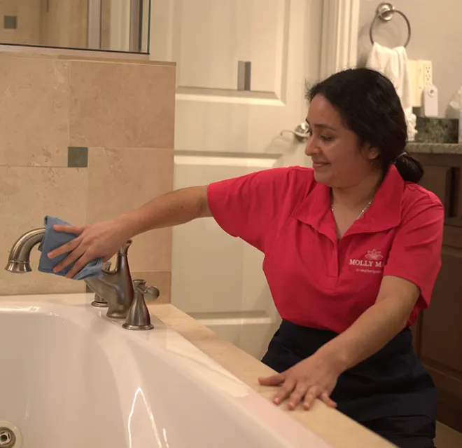 Molly Maid cleaning a bathtub faucet.